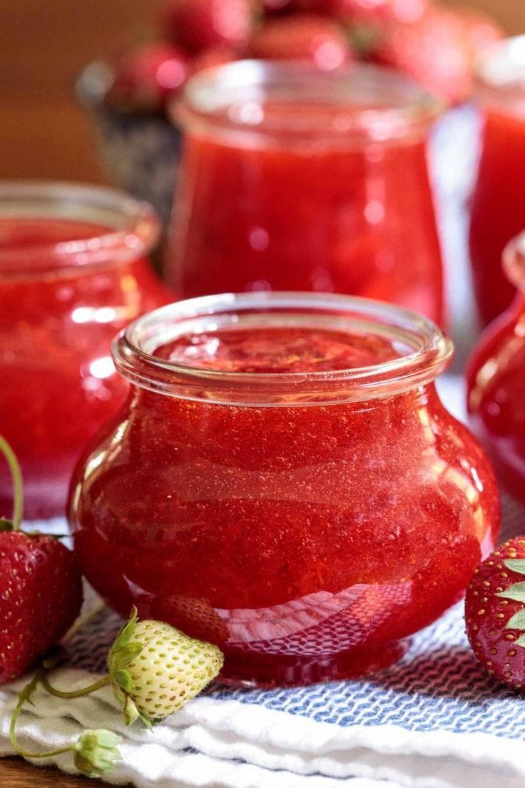 strawberry jam in a glass jar with strawberries around it