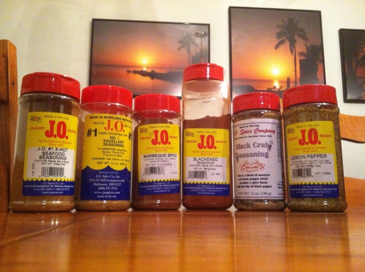 six jars of spices lined up on a wooden table with two pictures in the background