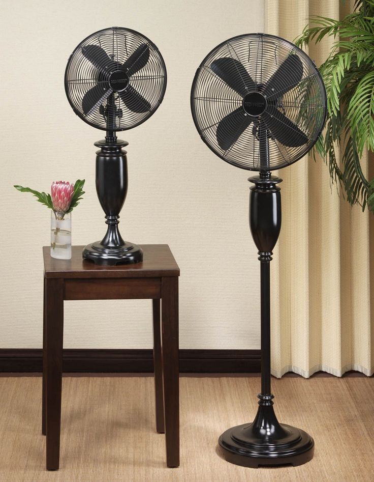 two black metal fans sitting on top of a wooden table next to a vase with flowers