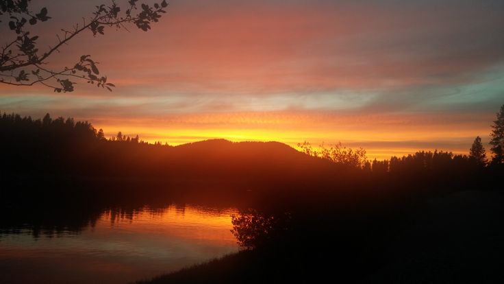 the sun is setting over a lake with mountains in the distance and trees around it