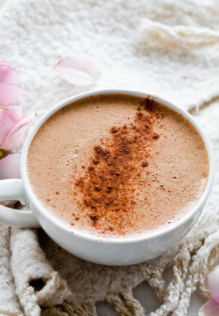 a cup of hot chocolate with cinnamon sprinkles on the top and pink flowers in the background