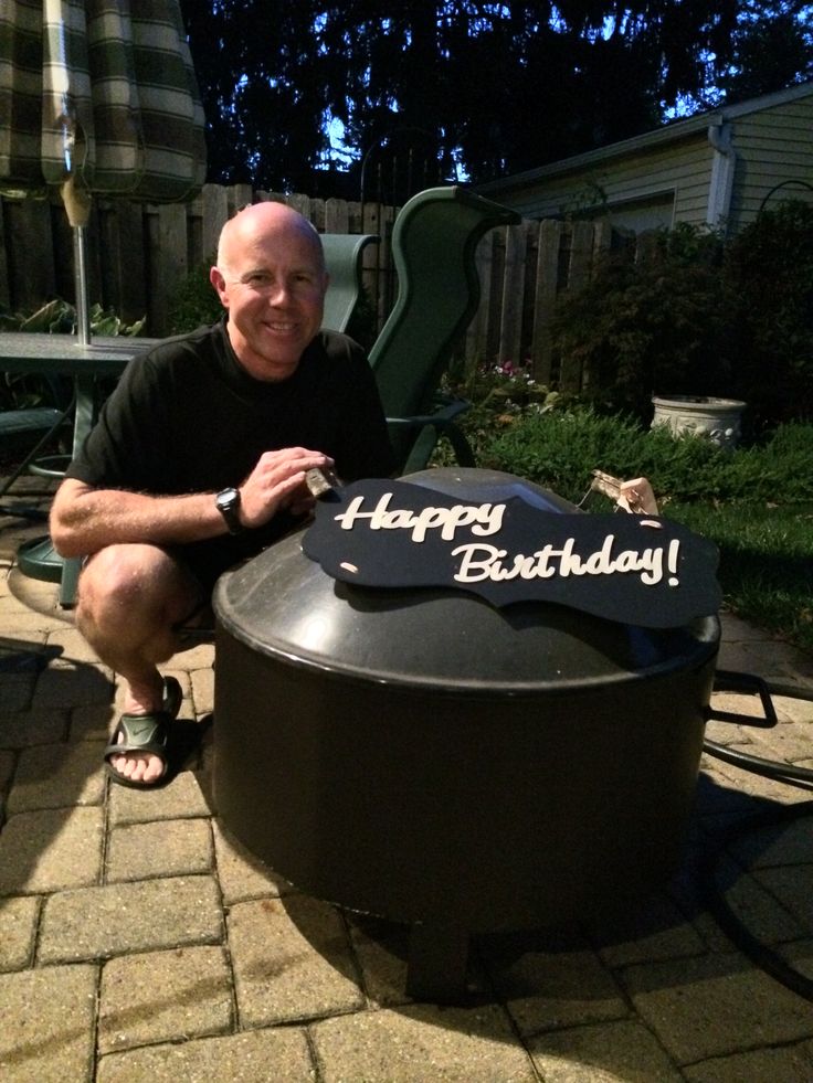 a man sitting in front of a birthday cake on top of a black table outside