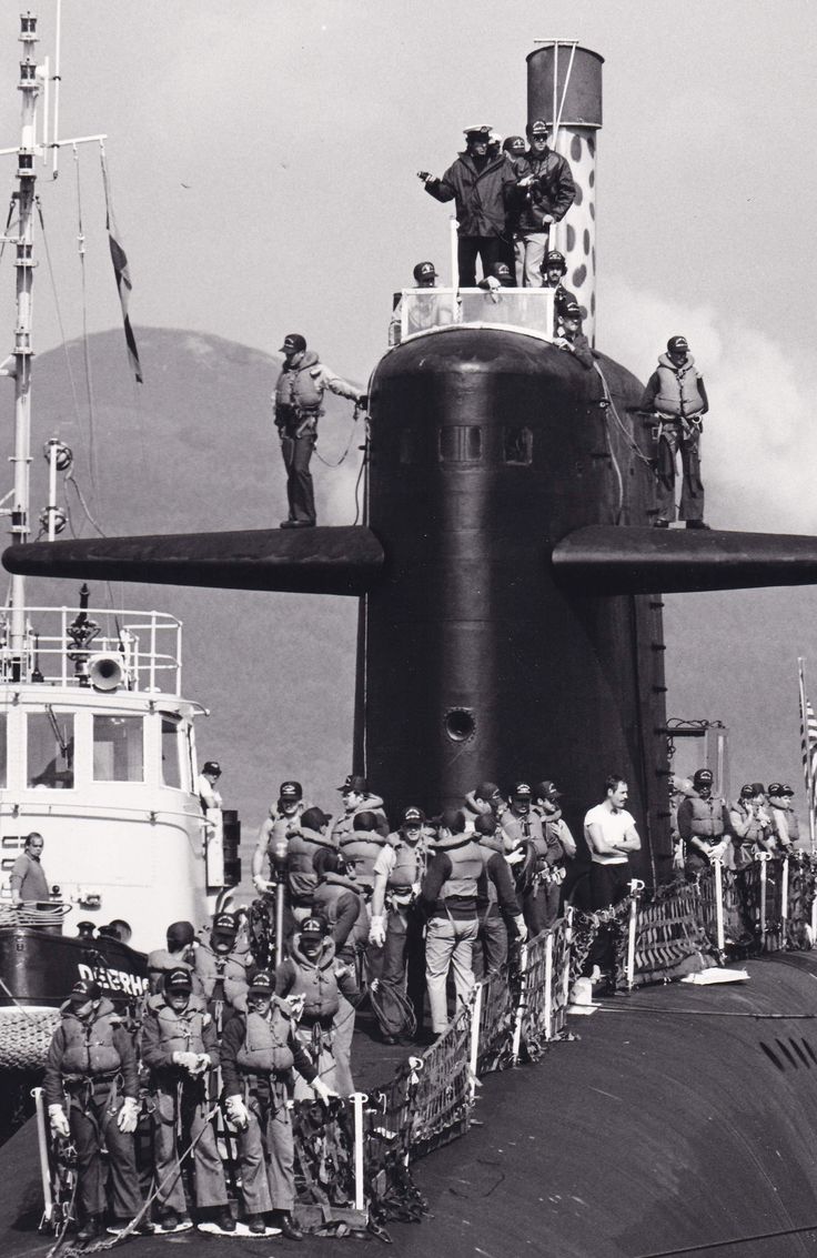 a group of people standing on the side of a boat next to a large submarine