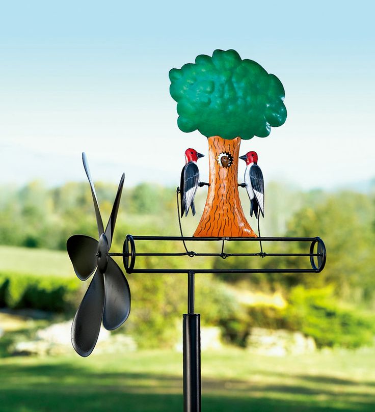 two birds are perched on top of a wind spinner with a tree in the background