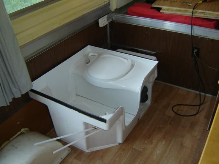 a toilet that is sitting in the middle of a room with wood flooring and windows