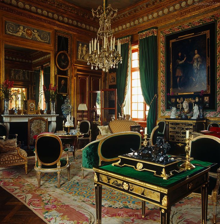 an ornately decorated living room with chandelier and green velvet sofas in the center