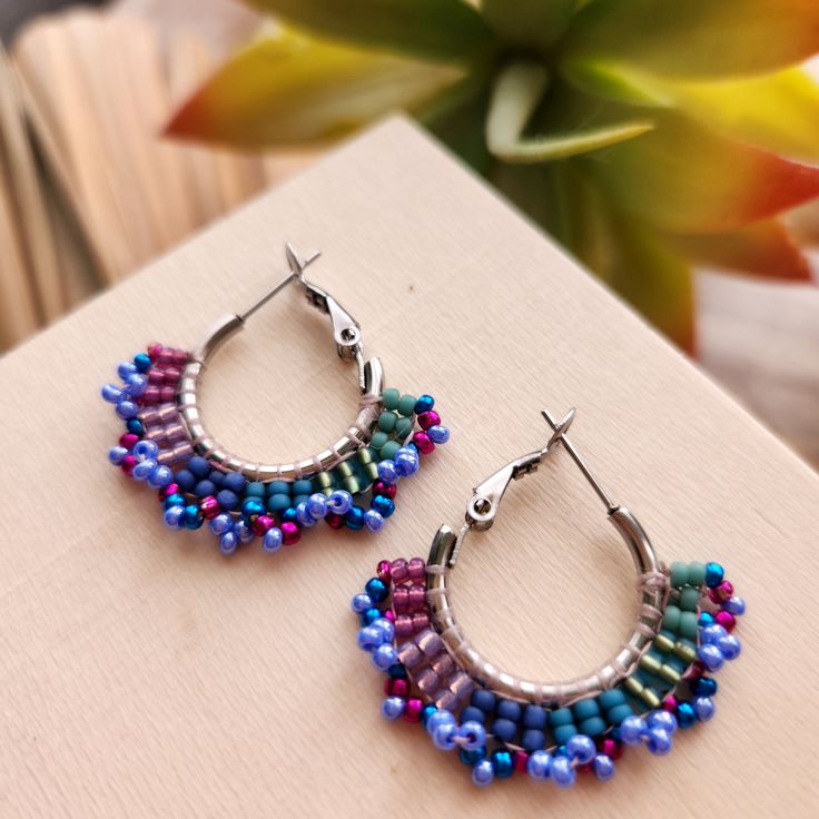 Stainless steel hoops encircled with glass beads in shades of fuscia, blue and iridescent violet. These handmade earrings add a bright pop of color to any outfit and make a great gift. 1 inch diameter stainless steel hoops.  Total diameter with beads = 1.25 inches. Purple Bohemian Hoop Earrings, Nickel-free Purple Hoop Earrings, Multicolor Metal Hoop Earrings With Ear Wire, Handmade Multicolor Metal Hoop Earrings, Handmade Purple Hoop Earrings, Handmade Small Purple Hoop Earrings, Purple Handmade Small Hoop Earrings, Nickel-free Purple Beaded Round Earrings, Multicolor Metal Hoop Jewelry