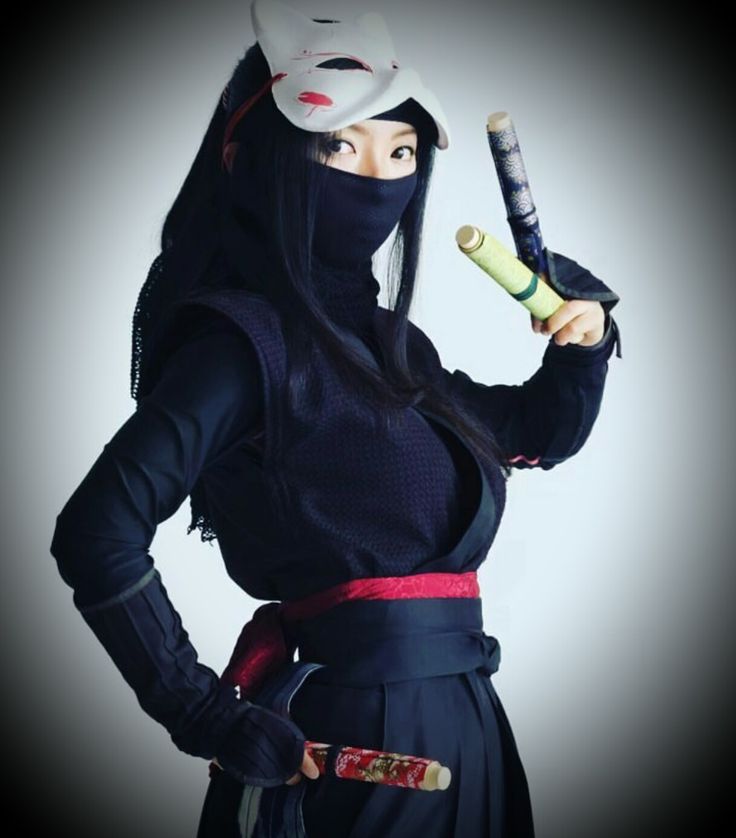 a woman dressed in ninja garb holding a baseball bat and wearing a mask on her face