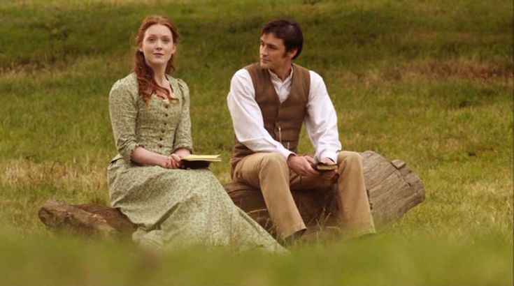 a man sitting next to a woman on top of a wooden log in a field