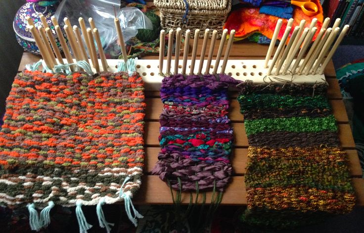 several knitted scarves and knitting needles on a wooden table in front of other items