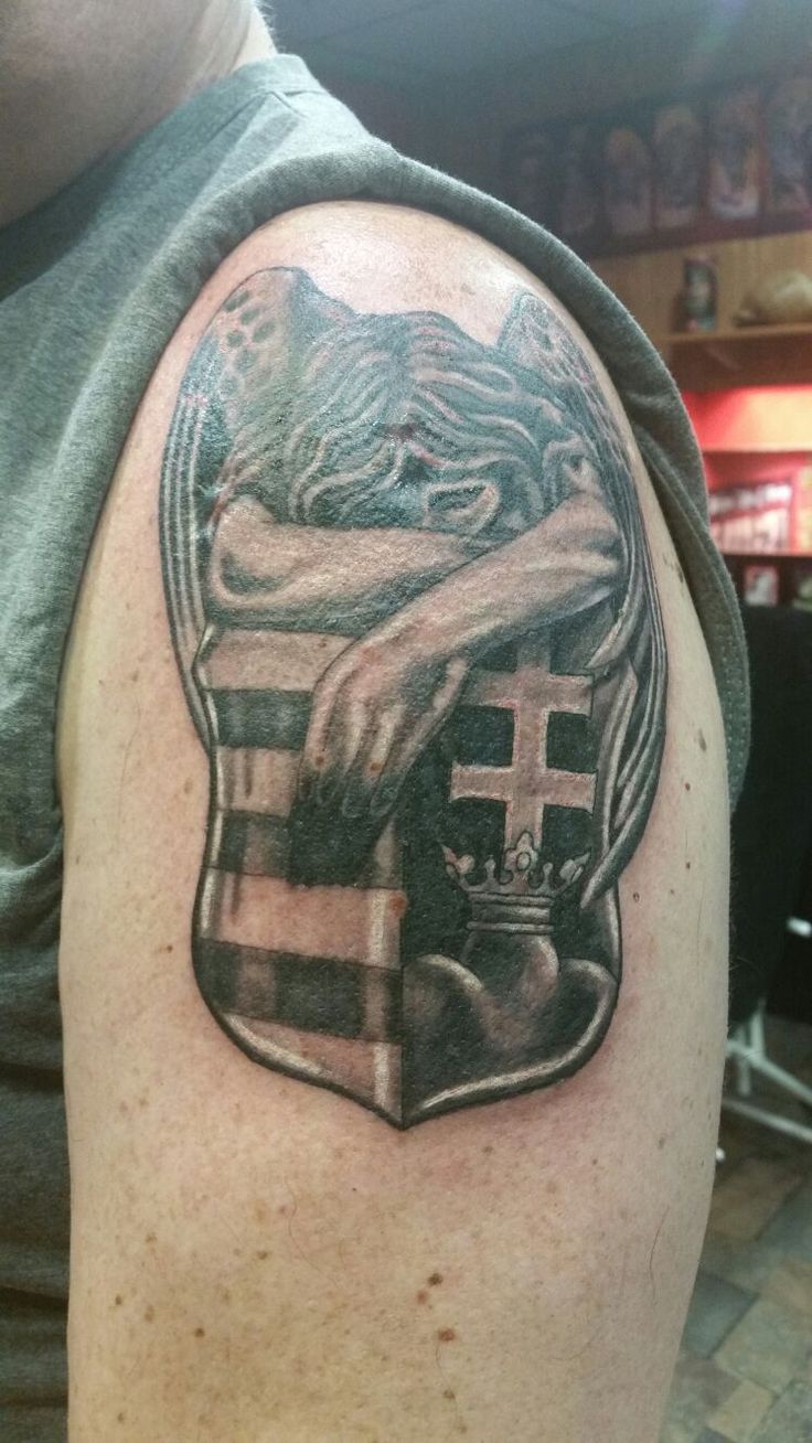 a man with a tattoo on his arm holding a cross and shield in front of him