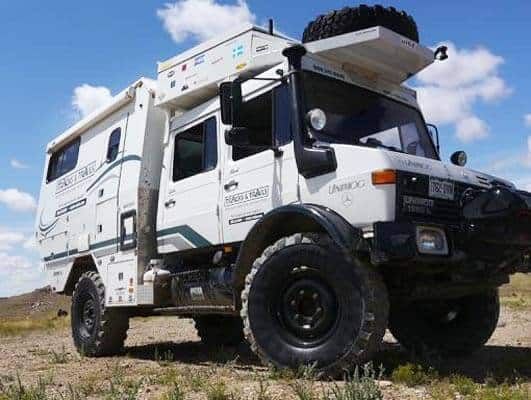 an off road vehicle parked on the side of a dirt road with a sky background