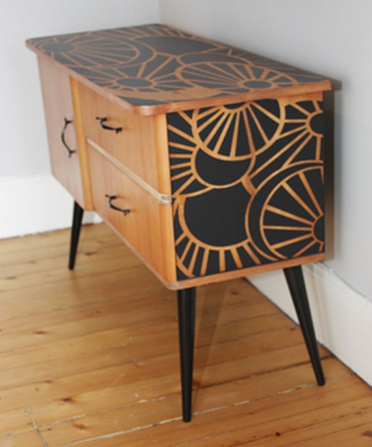 a wooden cabinet with black and gold designs on the front, next to a white wall