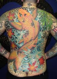 a man with tattoos on his back is standing in front of a blue wall and has an image of a goldfish