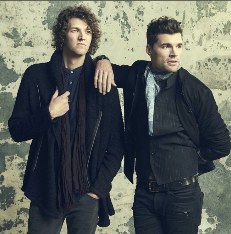 two young men standing next to each other in front of a wall with peeling paint