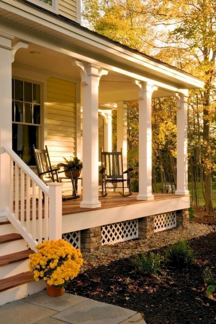 a porch with white pillars and yellow flowers on the front steps next to a house