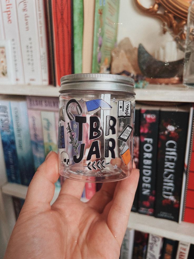 a person holding up a jar with letters on it in front of bookshelves