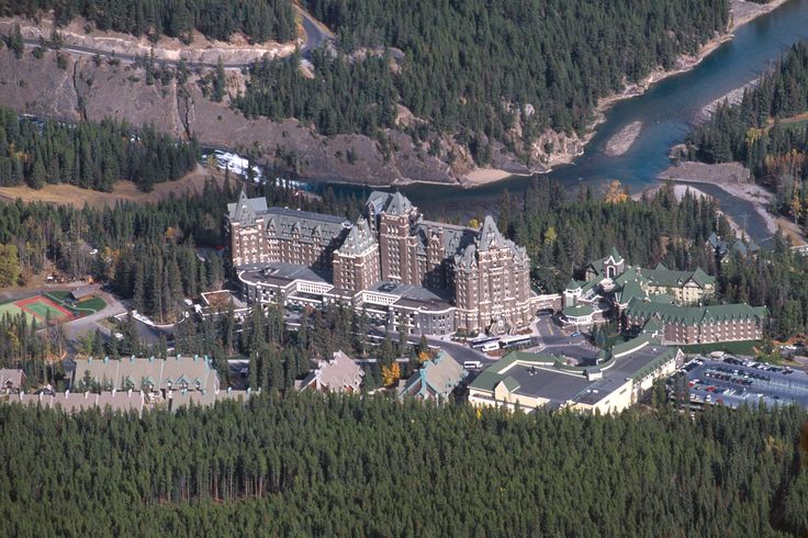 an aerial view of a large building surrounded by trees and mountains in the distance is a body of water