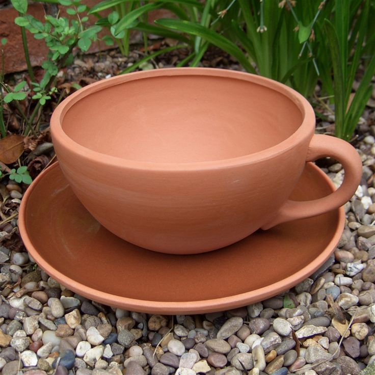 a clay cup and saucer sitting on top of a plate in the middle of gravel