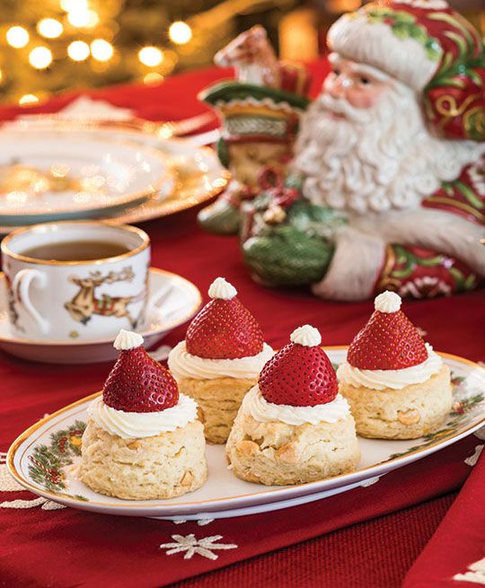 three small desserts on a plate with strawberries in the middle and santa clause figurines behind them