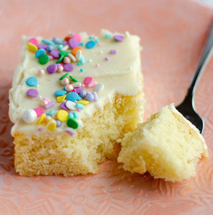 a piece of cake with white frosting and sprinkles on a pink plate