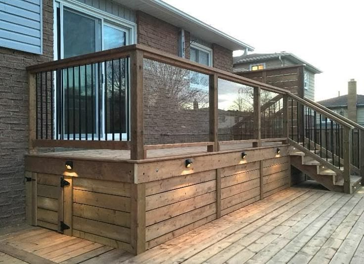 a wooden deck with lights on it next to a brick wall and stairs in front of a house