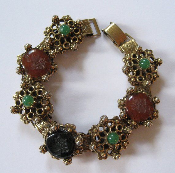 This is a wonderful vintage bracelet from the 1950's at my best estimate. This is a designer quality piece, but it is not marked or signed. Done in the style of Florenza, Art, and Goldette, this revival style bracelet features black and carnelian glass cabochons with Grecian gods or goddesses "carved" into the tops. These are probably molded glass intaglios. The black and carnelian stones are accented with green round ballotini, also glass. The bracelet is gold plated. The bracelet is 7 inches l Thomas Charley Jewelry, Luxury Intaglio Bracelets, Formal Metal Bracelet With Vintage Charm, Vintage Round Bracelet With Jewels, Vintage Jeweled Bracelets For Collectible, Costume Jewelry Jubilee Bracelet, Retro Jeweled Bracelet For Formal Occasions, Retro Jeweled Bracelets For Formal Occasions, Adjustable Vintage Bracelet Embellished