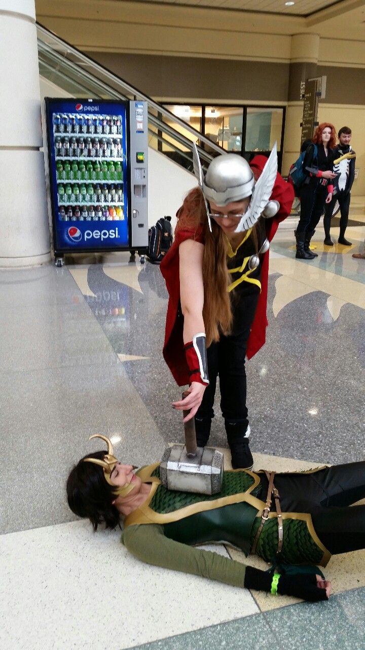 a woman dressed as thor and loki in an airport lobby with another woman on the floor