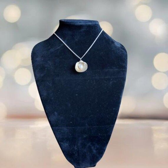 Embrace the beauty of the ocean with our handcrafted Seaside Elegance necklace, a stunning piece that captures the essence of the shore. This necklace features a natural seashell pendant, carefully selected for its unique shape and intricate patterns, paired with a lustrous freshwater pearl that adds a touch of elegance. Each necklace is lovingly handcrafted, ensuring that no two pieces are exactly alike--just like the treasures you find on the beach. The combination of organic elements and time Ocean-inspired Shell Necklaces For Gifts, Shell-shaped Pearl Pendant Jewelry, Shell-shaped Jewelry With Pearl Pendant, Shell Pendant Charm Necklaces For Gifts, Shell Jewelry With Pearl Pendant, Ocean-inspired Shell-shaped Jewelry Gift, Ocean-inspired Shell-shaped Pearl Pendant Jewelry, Shell Pendant Jewelry With Pearl Charm, Ocean-inspired Mother Of Pearl Shell Necklace As Gift