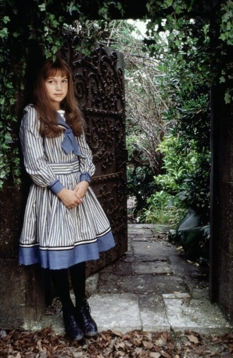 a woman standing in front of an iron gate with leaves on the ground around her