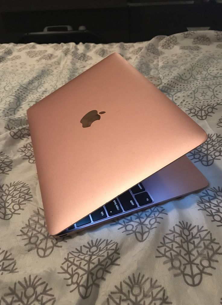 two apple laptops sitting on top of each other on a bed with floral sheets