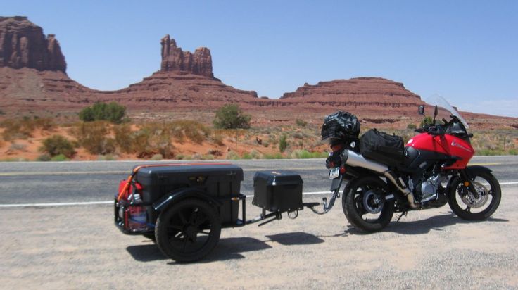 a motorcycle parked next to a trailer on the side of the road with mountains in the background