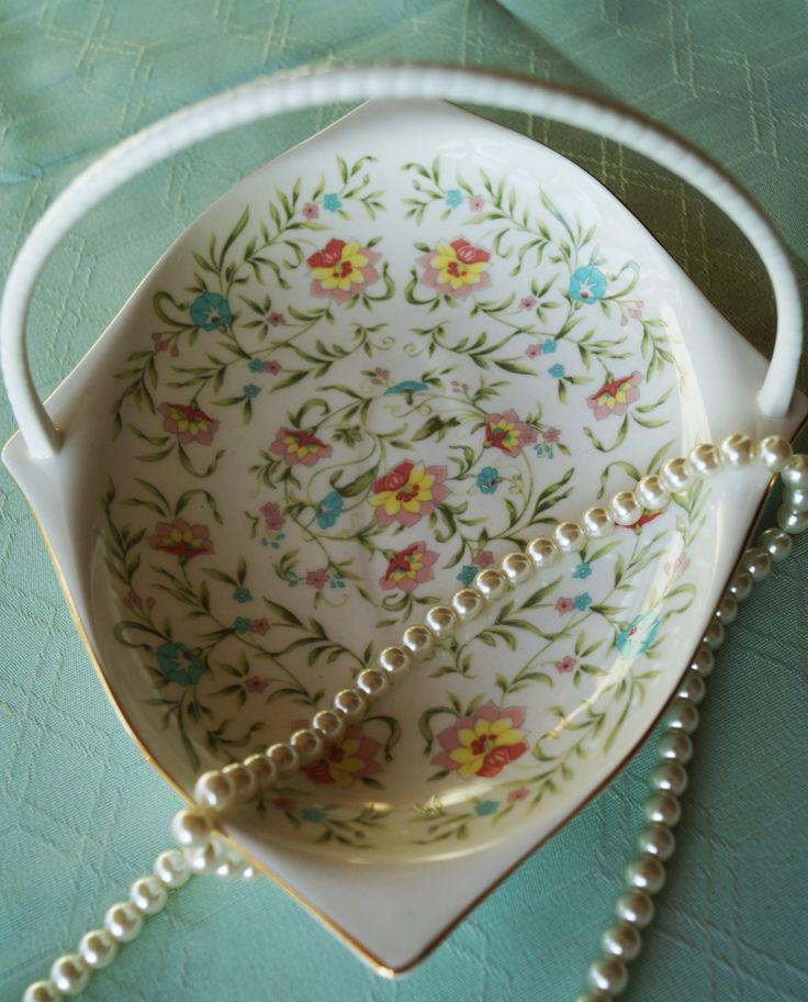 a white bowl with flowers and pearls on the bottom is sitting on a green tablecloth