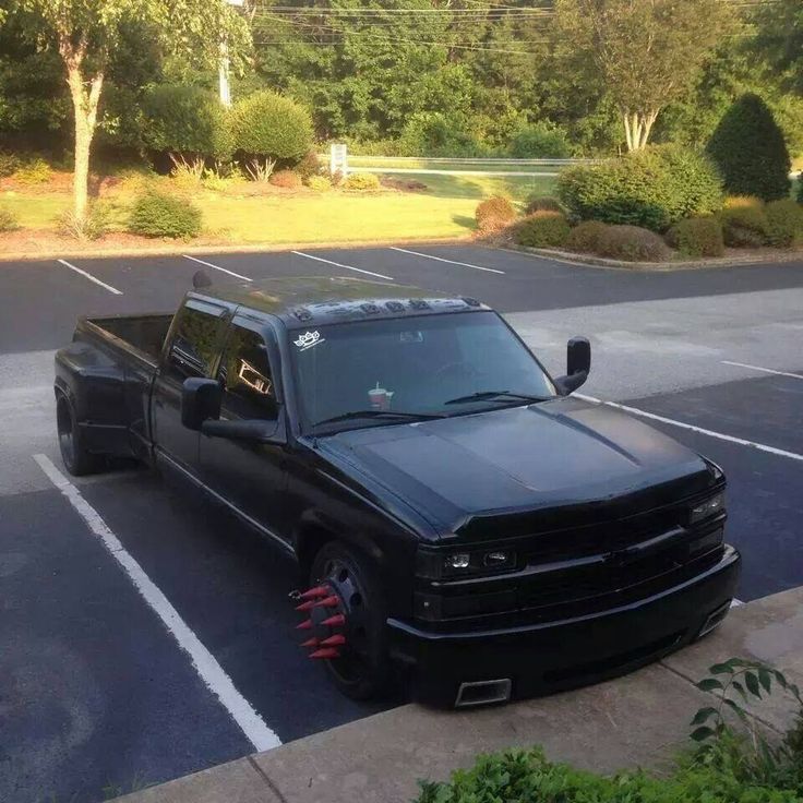 a black pickup truck parked in a parking lot next to a tree and shrubbery