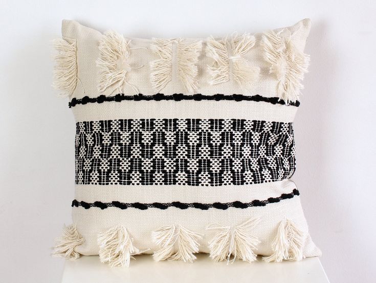 a black and white pillow with tassels on the bottom is sitting on a table