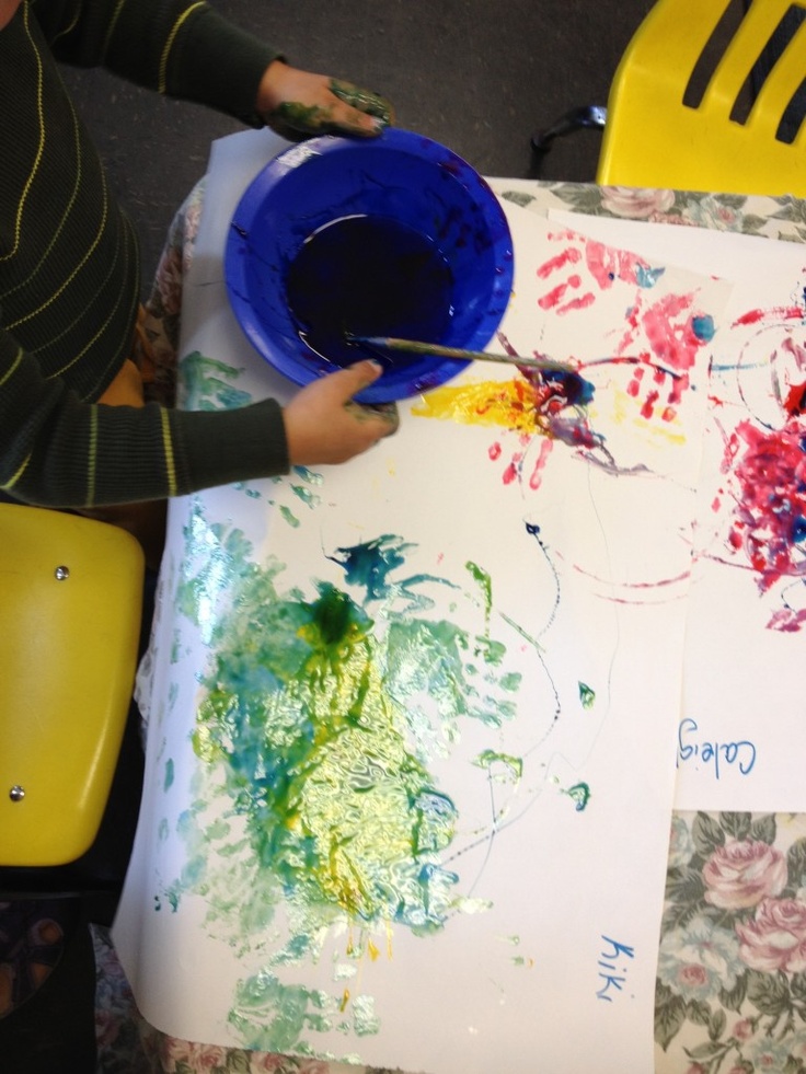 a child is painting on paper with paintbrushes and watercolors in front of them