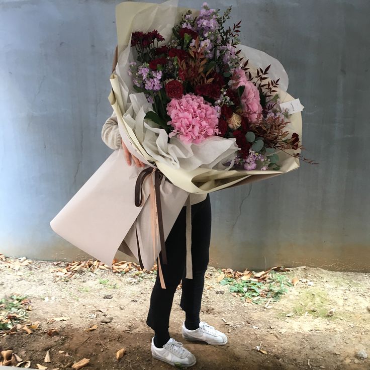 a woman holding a bouquet of flowers in her hands while wearing white tennis shoes and carrying a pink bag