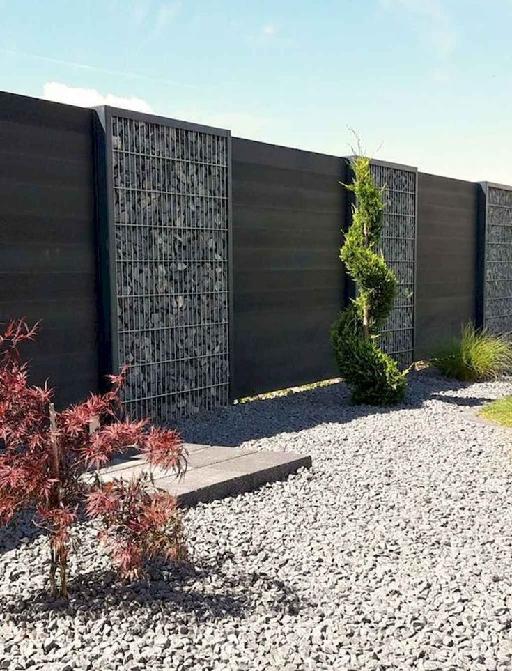 a garden area with gravel and plants next to a black fenced in area that has stones on the ground