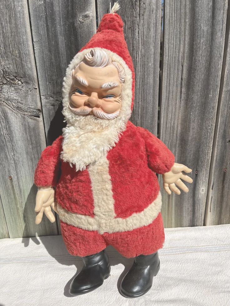 an old fashioned santa clause doll standing next to a wooden fence