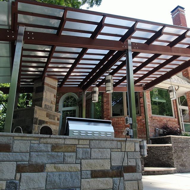 an outdoor grill area with stone wall and pergolated roof over the bbq