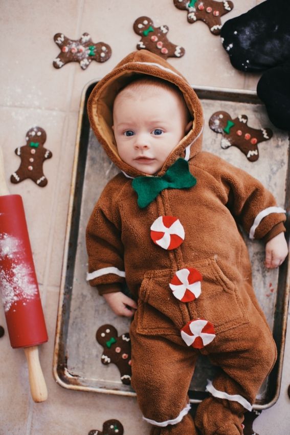 a baby dressed in a gingerbread outfit laying on a baking pan with cookies around it