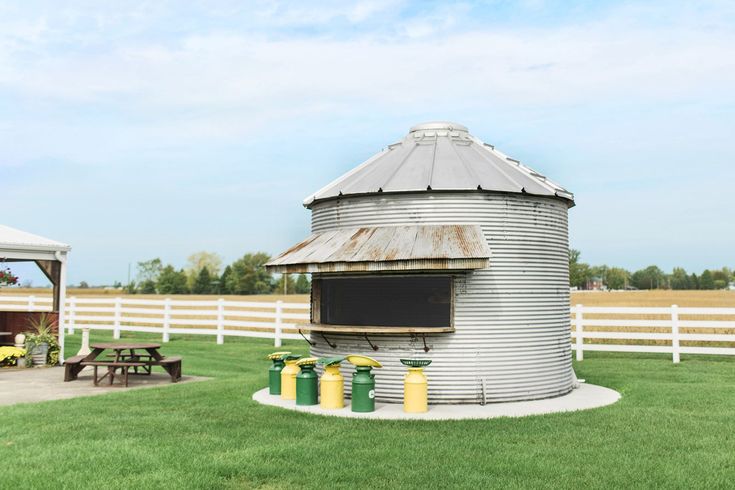 a large metal silo sitting on top of a lush green field next to a white fence