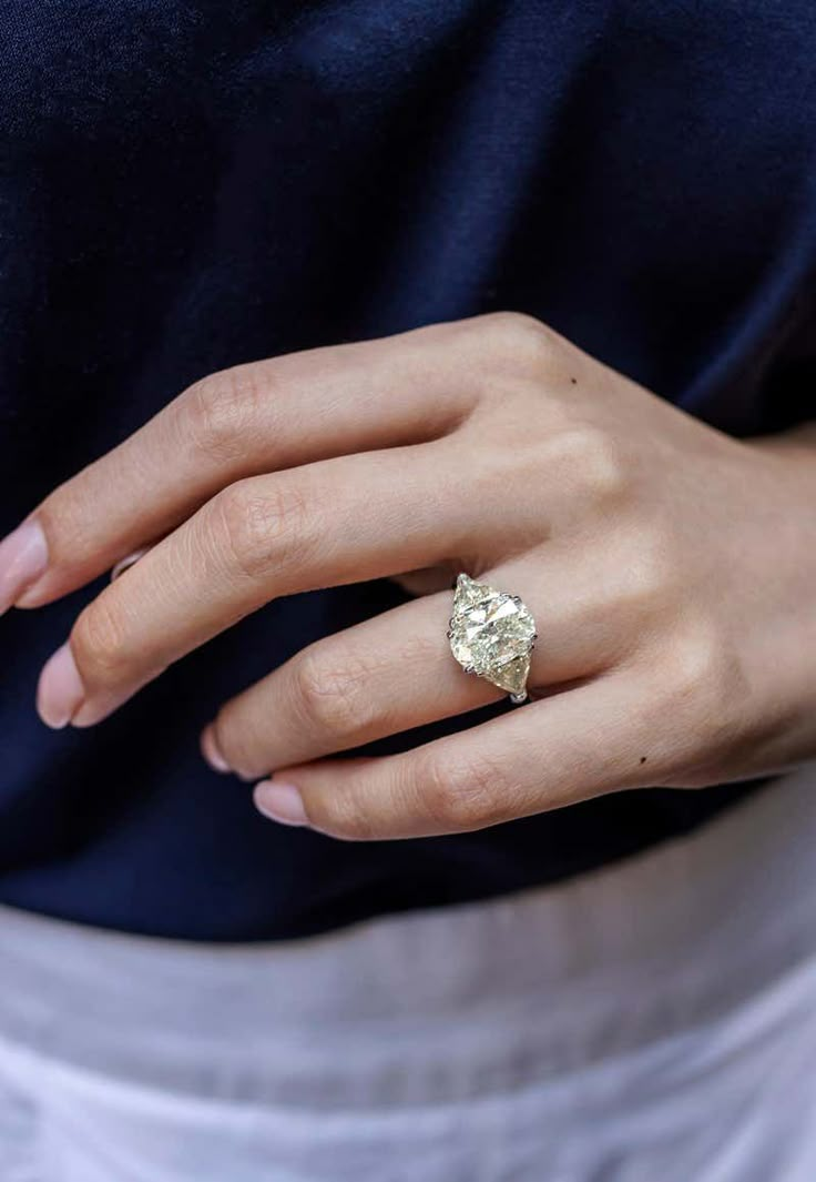 a woman's hand with a diamond ring on her left hand, wearing a blue shirt