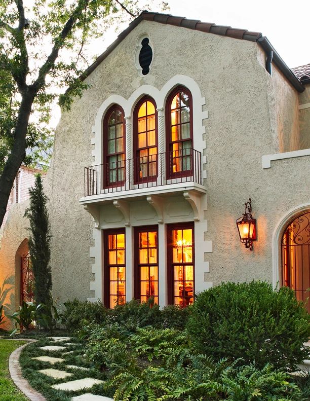 a white house with lots of windows and plants in the front yard, surrounded by greenery