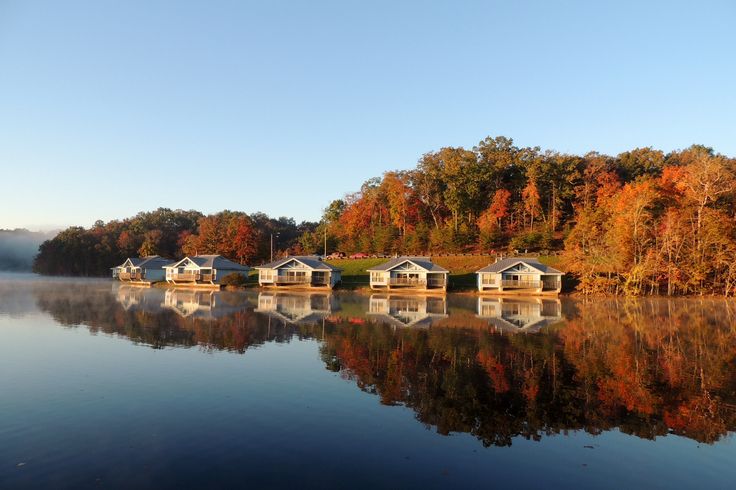 houses on the shore of a lake surrounded by trees in fall colors, with water reflecting them