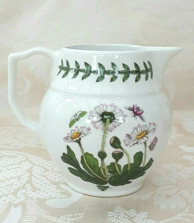 a white pitcher with flowers painted on the side and green leaves in the middle, sitting on a lace tablecloth