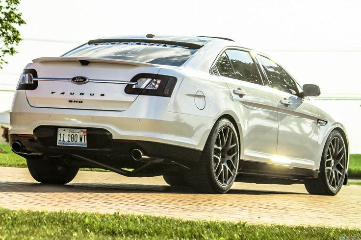 the rear end of a white car parked in front of a tree and grass area