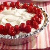 a pie with whipped cream and cherries on top sitting on a pink table cloth