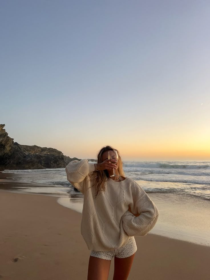 a woman standing on top of a sandy beach next to the ocean with her hands behind her head