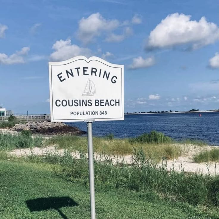 a sign that is in the grass by the water and some sand on the ground